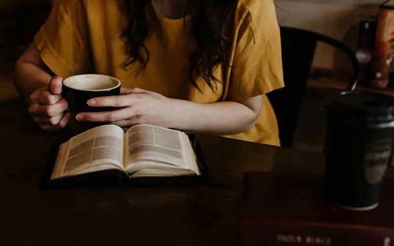 A woman in a yellow shirt with a mug of coffee and an open Bible