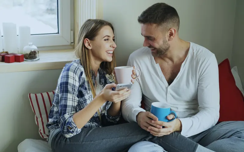 A young couple laughing over mugs of coffee on a couch