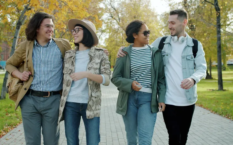 Four friends walking together through a sunny park