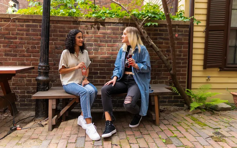 Two women talking on a bench in a sunlit courtyard