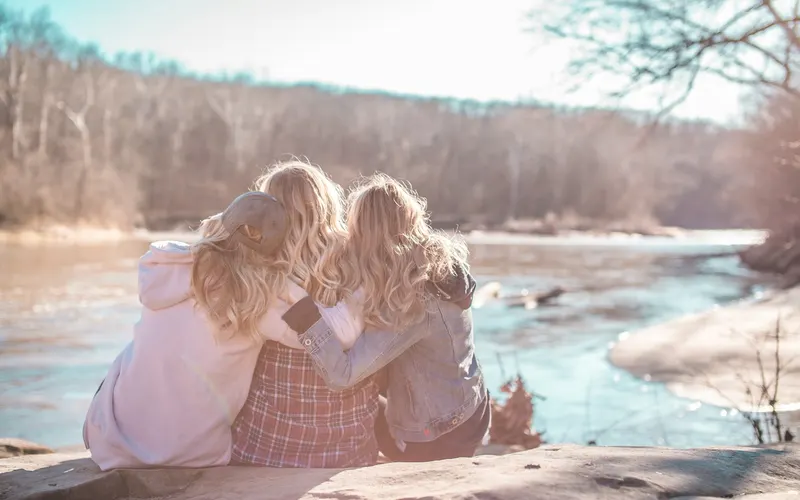 Three friends sitting close together beside a river