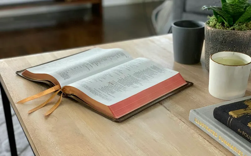 An open Bible on a coffee table beside two mugs