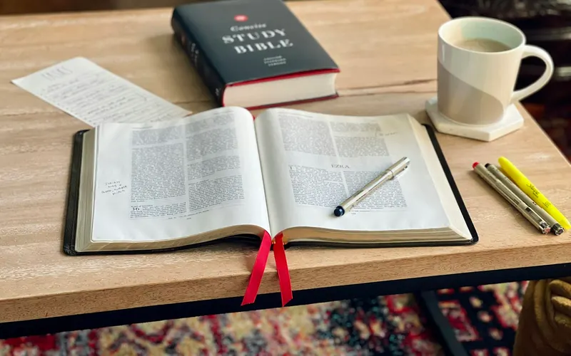 A study Bible open beside notes, pens, and a mug