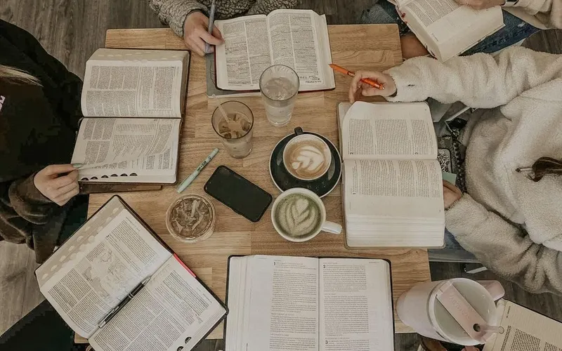 Bibles, notebooks, and coffee spread across a study table, seen from above