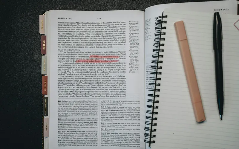 An open Bible beside a spiral notebook and pens, from above
