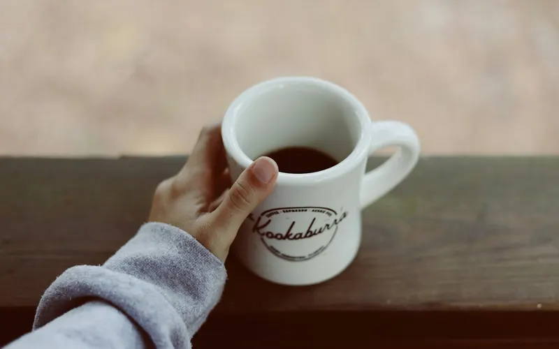 A hand holding a mug of coffee on a porch rail