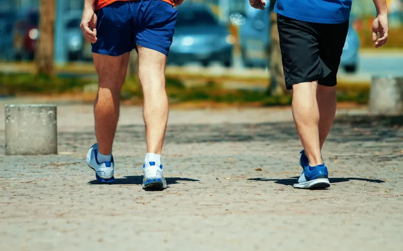 Two men in workout gear walking a sunny sidewalk
