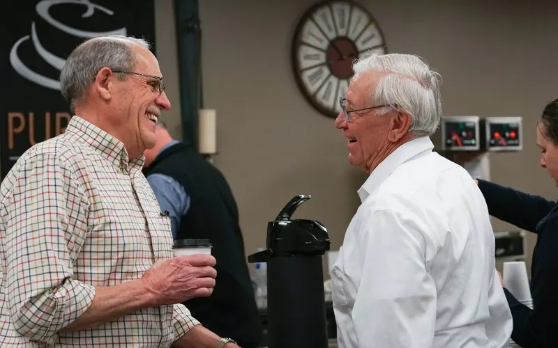 Two older men laughing together over coffee