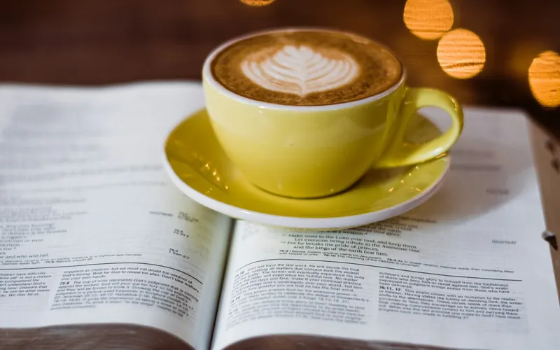 A latte in a yellow cup resting on an open Bible