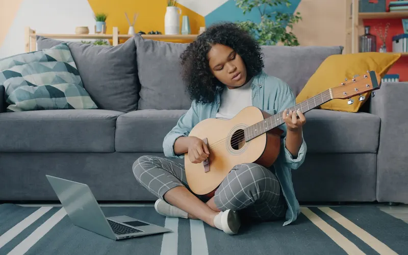 A woman playing an acoustic guitar on a living room couch