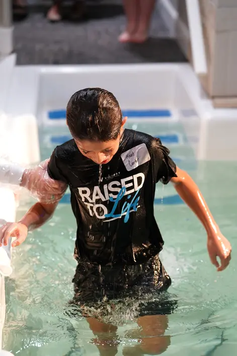 A young man in the baptism pool in his Raised to Life shirt