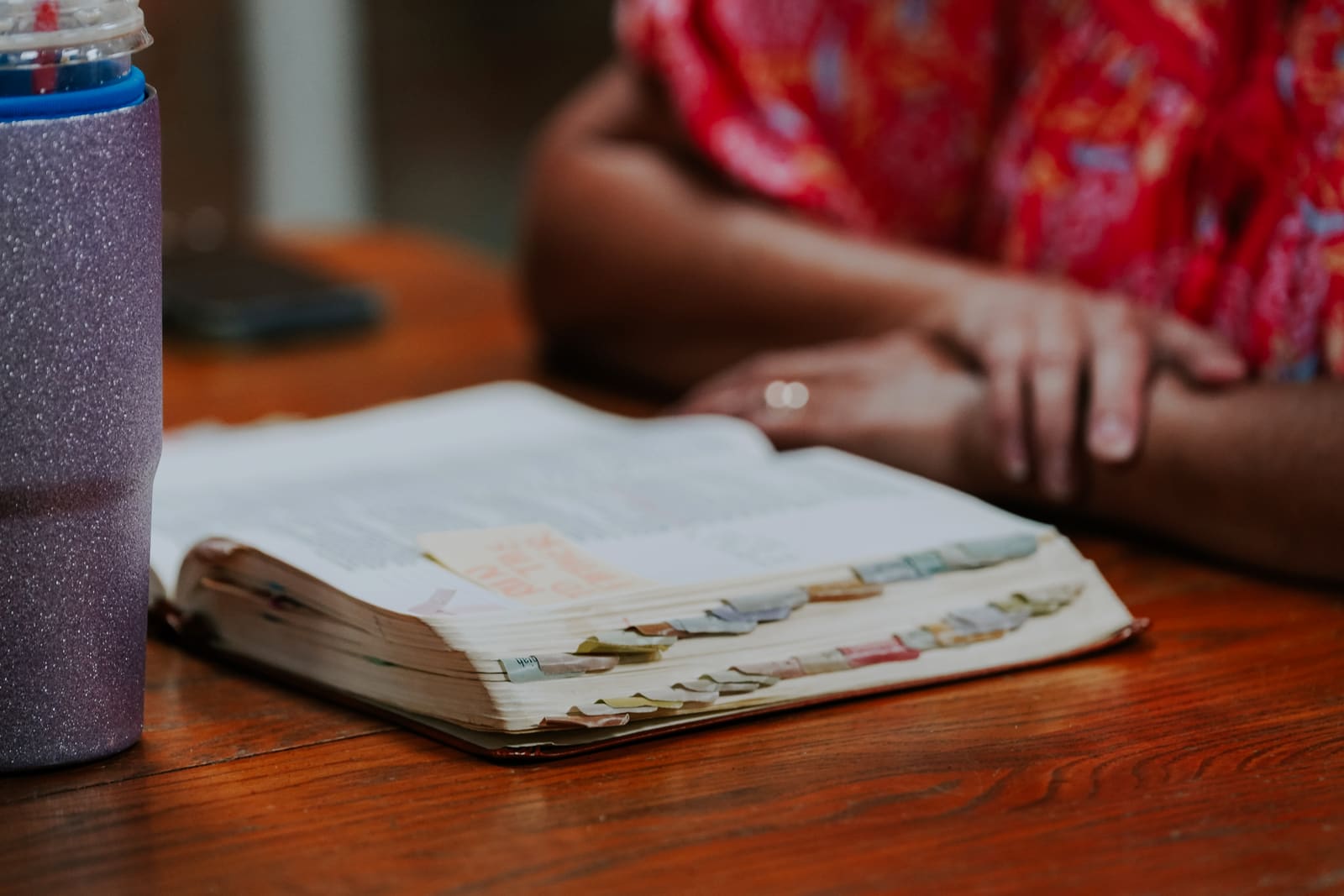 A worn, tabbed Bible open on a table with a woman's hands resting beside it