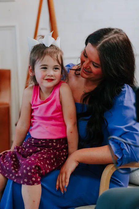 A woman and a little girl cheek to cheek, both laughing