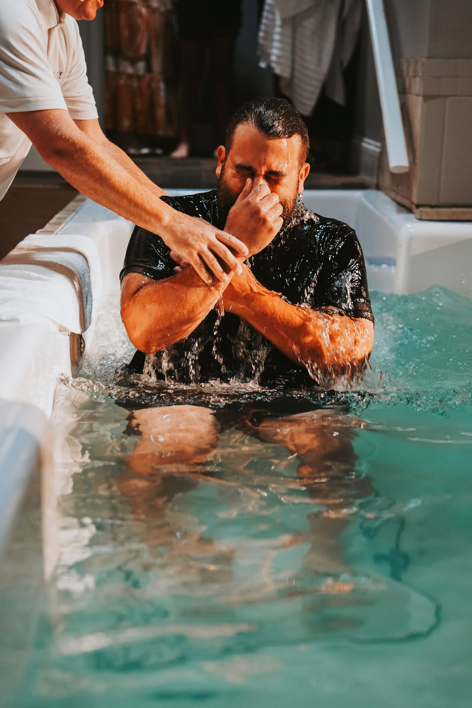 A man rising out of the baptistry water at Victory, hands to his face