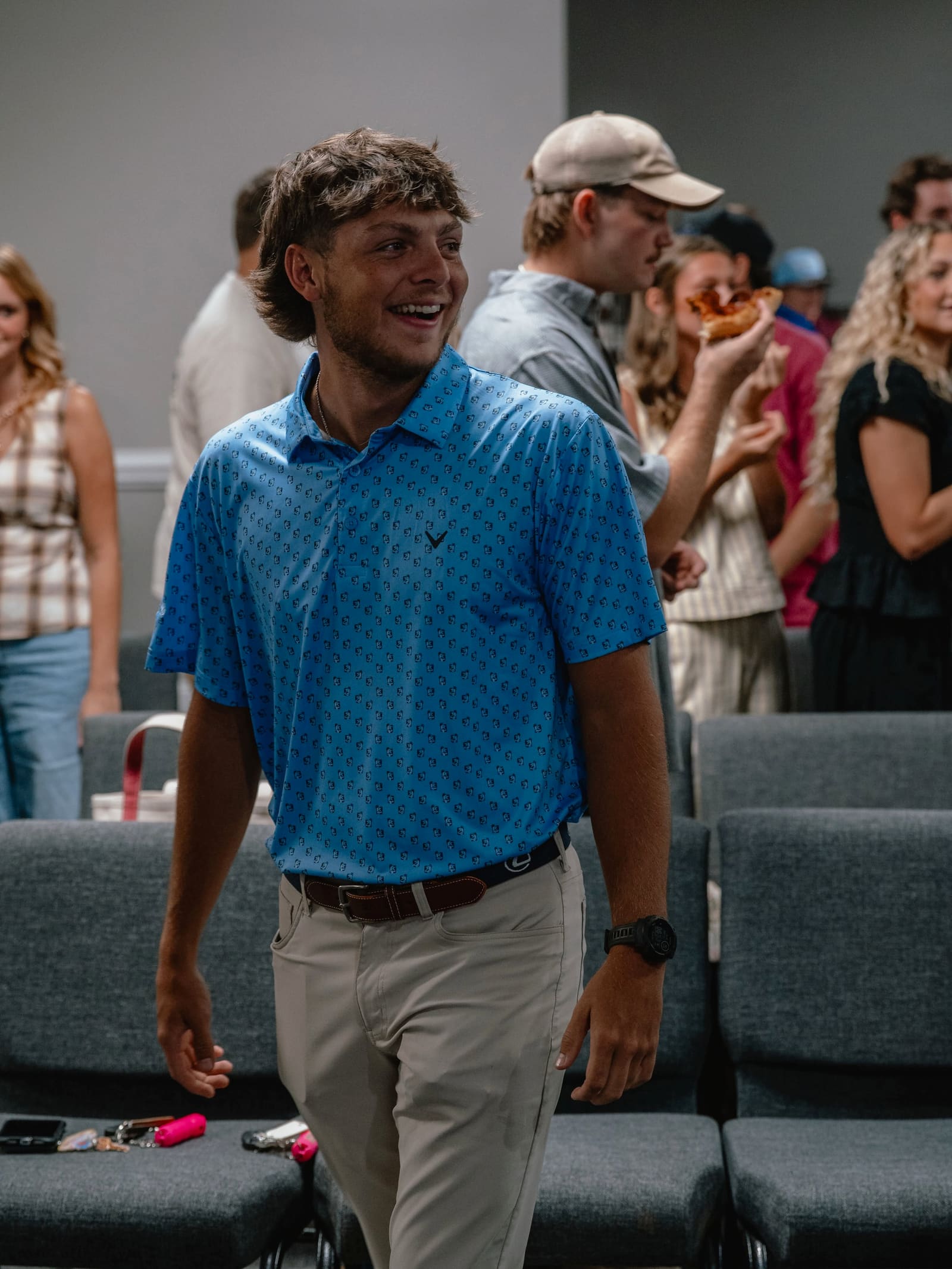 A young adult smiling as he walks between rows of chairs at a Victory gathering