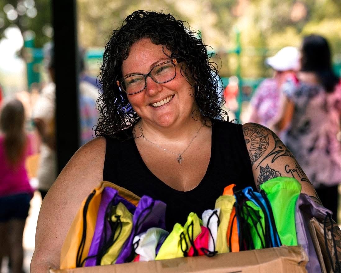 A Dream Team member smiling as she carries a box of colorful supply bags at an outdoor giveaway