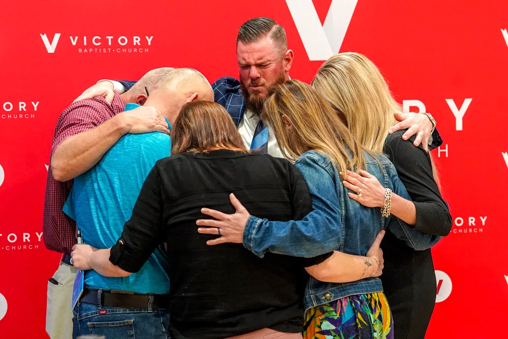 Pastor CT praying in a huddle with members in front of the red Victory backdrop