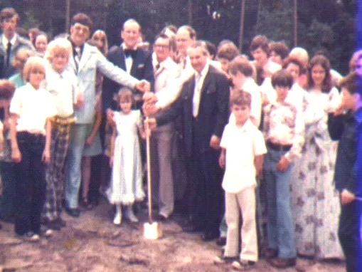 The congregation gathered around the groundbreaking shovel in the cleared woods