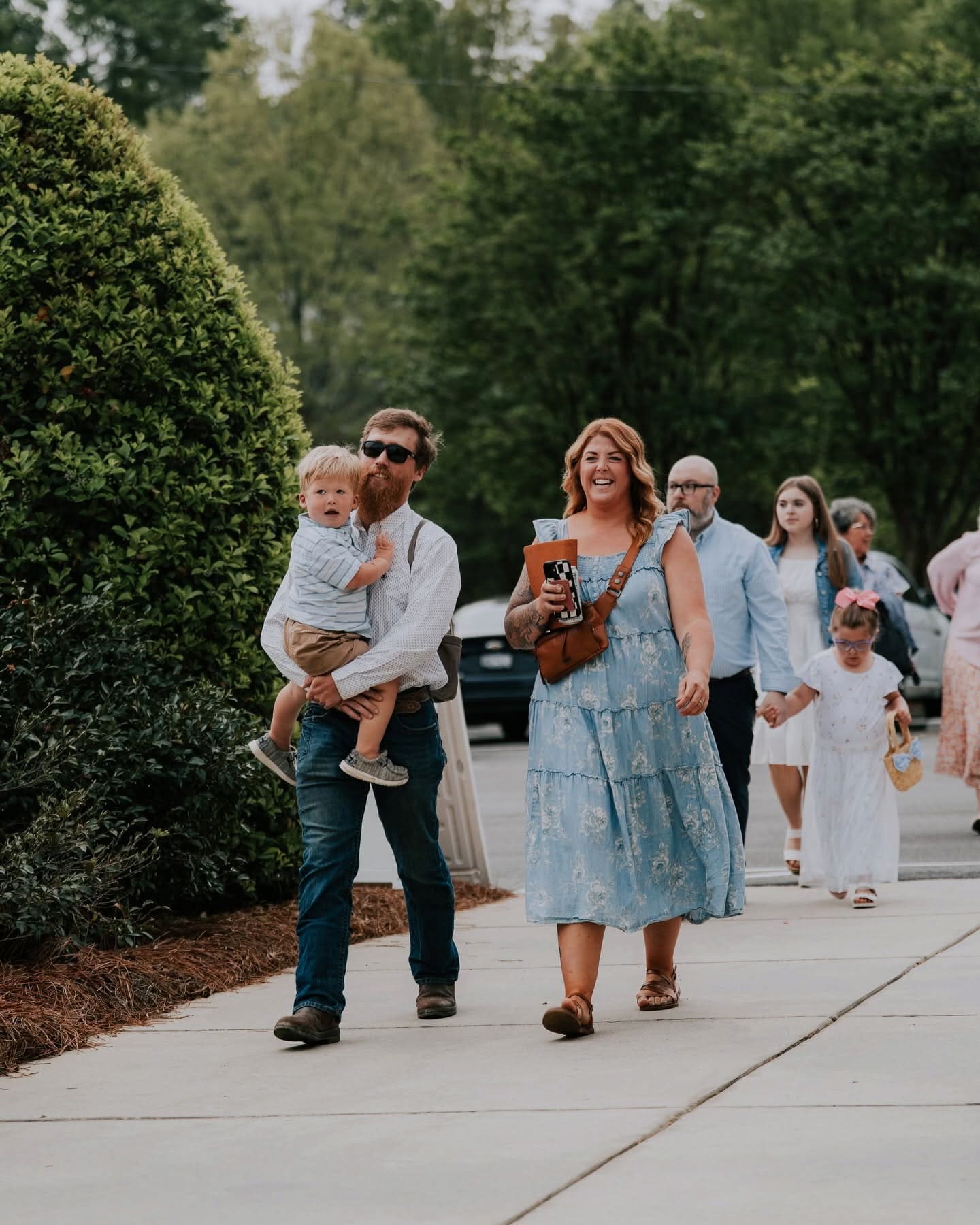 A family walking up the sidewalk to the church doors on a Sunday morning, their toddler riding on dad's arm