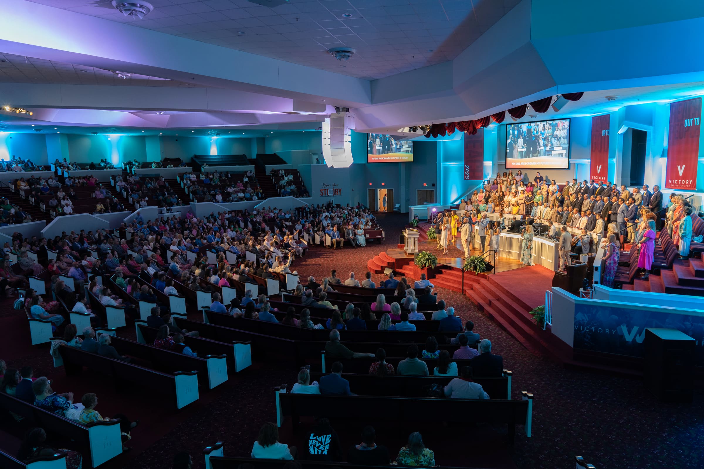The Victory auditorium full for a Sunday service, seen from the back of the room with the platform lit