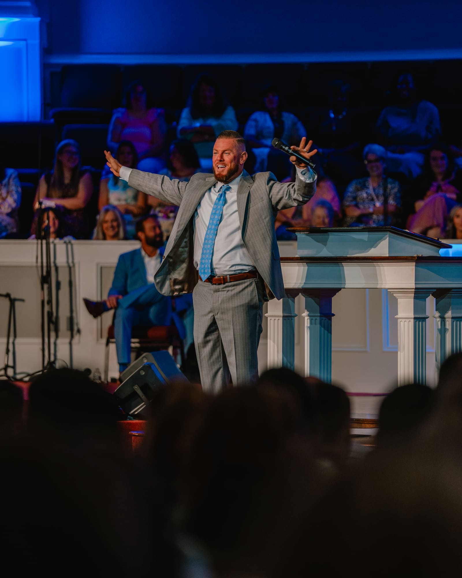 Pastor CT preaching with both arms open on the platform during a Sunday service