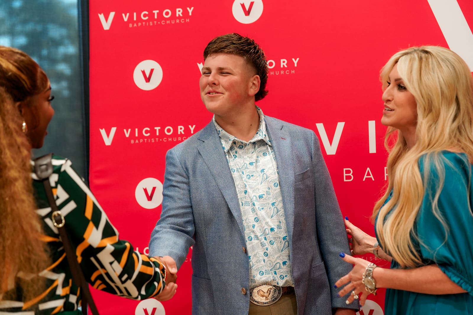 Members greeting one another with a handshake in front of the Victory backdrop after a service