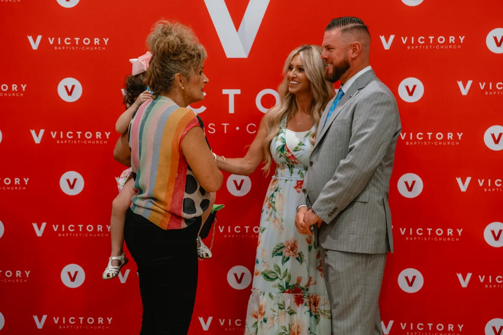 Becky and Pastor CT greeting a grandmother holding a little girl at the Victory backdrop
