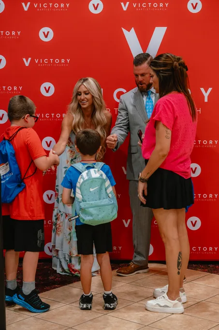 Pastor CT and Becky greeting two boys with backpacks at the Victory backdrop