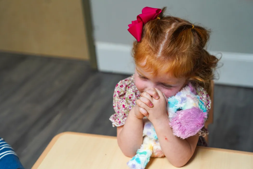 A toddler squeezing a stuffed unicorn at a table