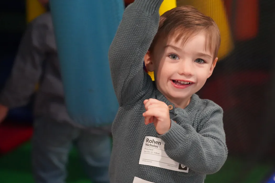 A toddler in a name tag grinning in the Victory Nursery
