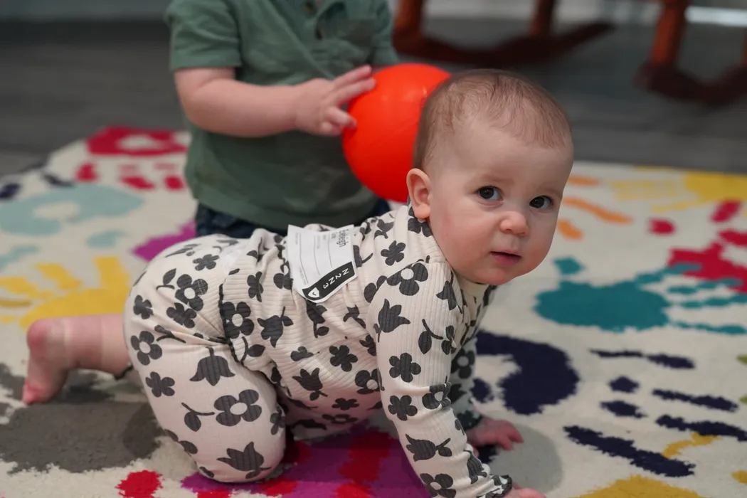 A baby crawling across the nursery rug toward a red ball