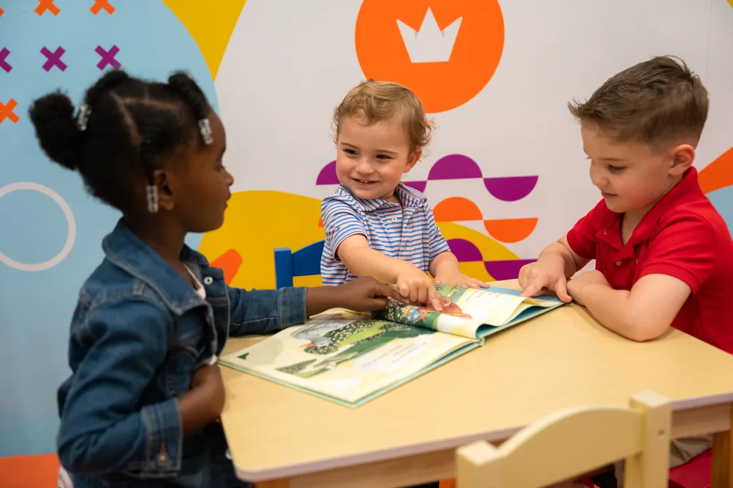 Three kids reading a picture book together at a table in the Victory Kids room