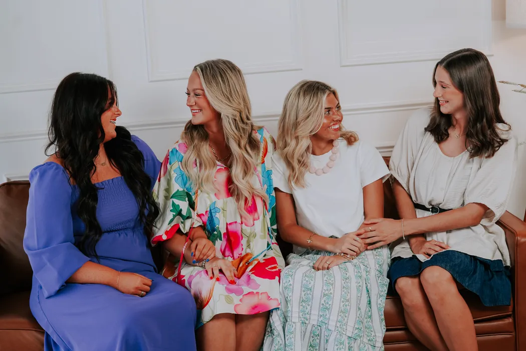 Four young women laughing together on a couch