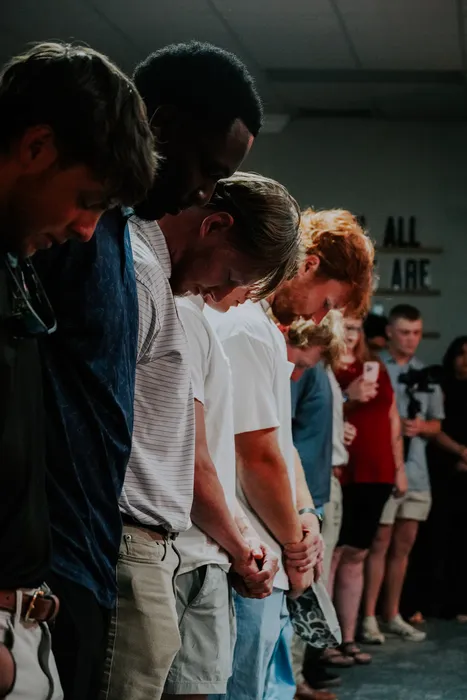 Young adults praying together with their heads bowed