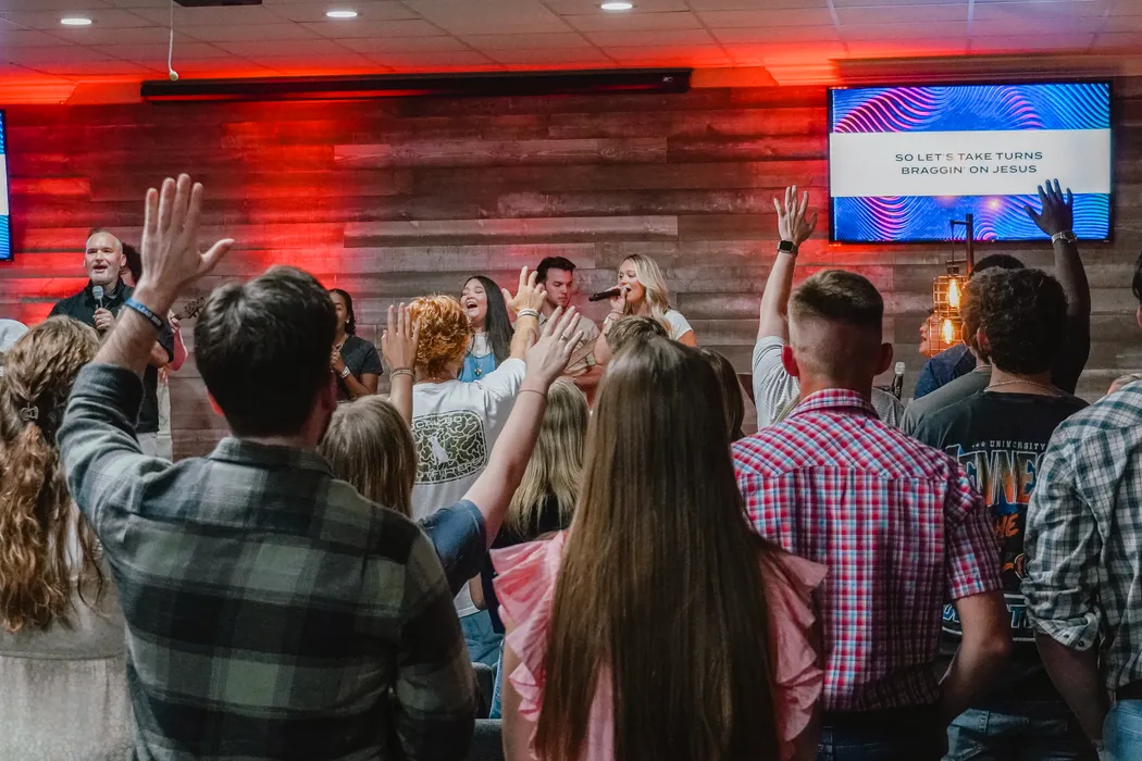 Young adults with hands raised at a Victory Young Adults gathering