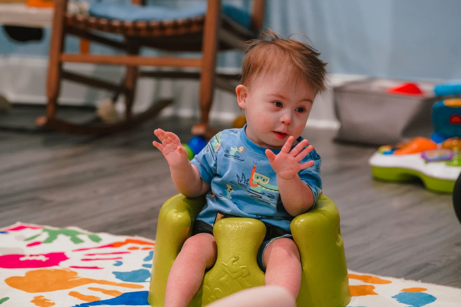 A baby clapping in a green floor seat in the Victory Nursery