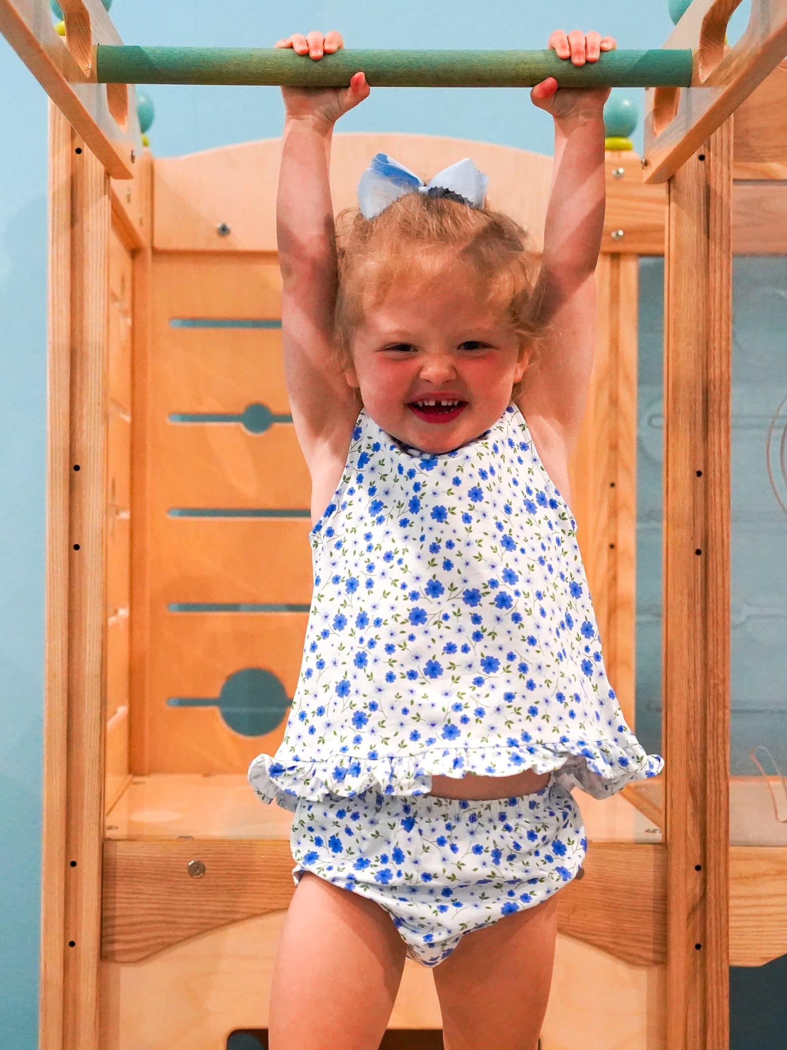 A laughing toddler hanging from the play-gym bar in the nursery play area