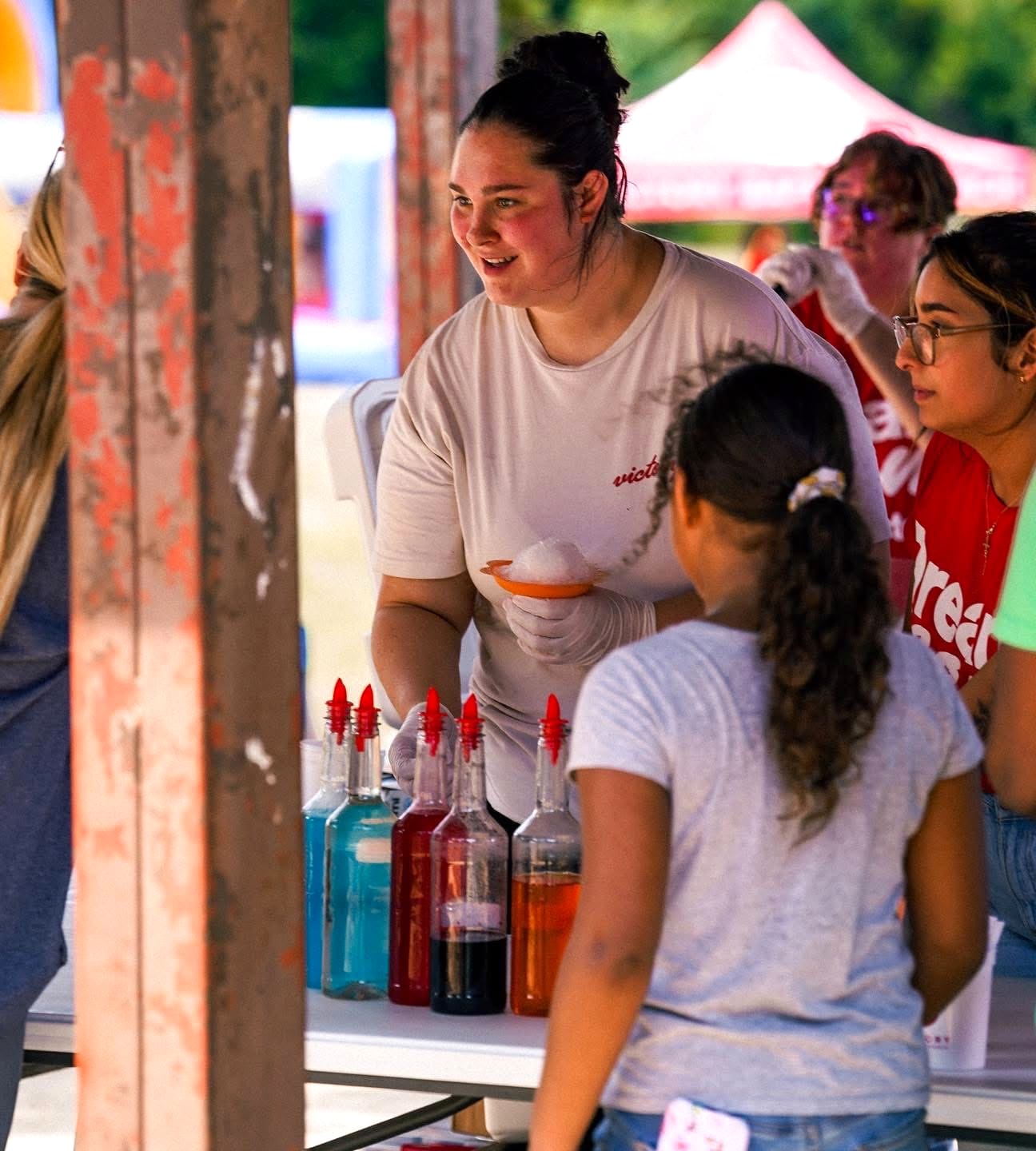 A volunteer handing a shaved-ice cup to a child under the outreach tent