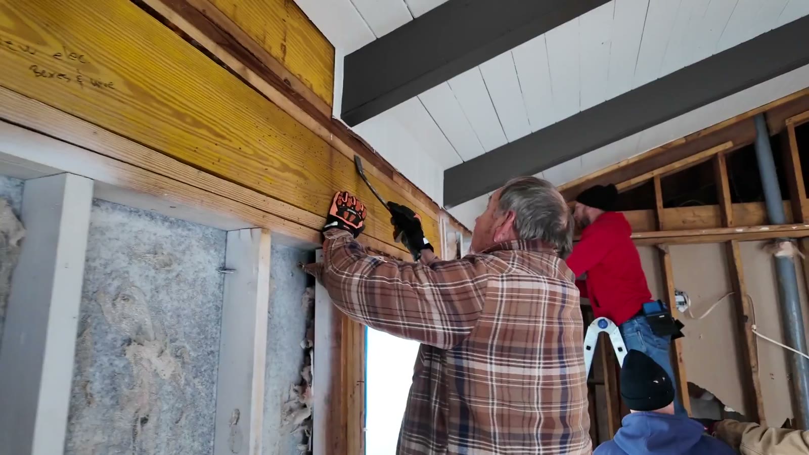 Volunteers in work gloves repairing an exposed stud wall on a build project