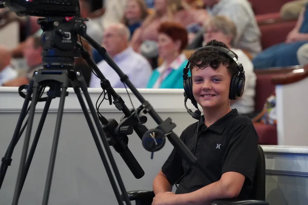 A young production team member in headphones running a camera during a service