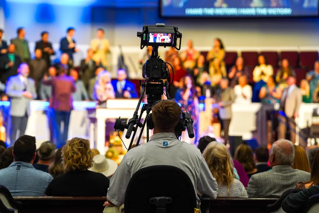 A camera operator filming the service from the back of the sanctuary