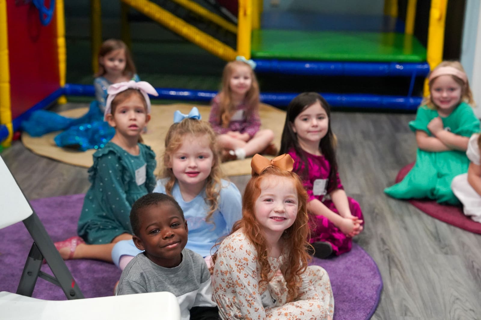 A group of preschoolers sitting together on the rug in the Victory Kids room, most of them smiling at the camera